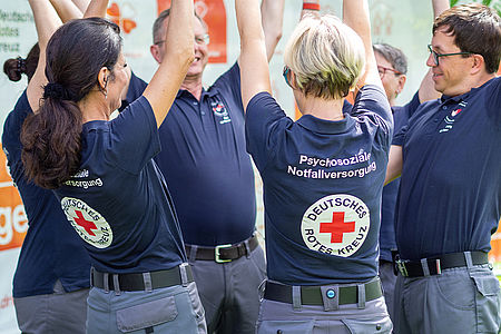 Mehrere DRK-Mitarbeiter stehen zusammen und strecken ihre Hände in die Höhe.