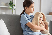 Trauriges Mädchen mit Stoffhase sitzt auf dem Sofa