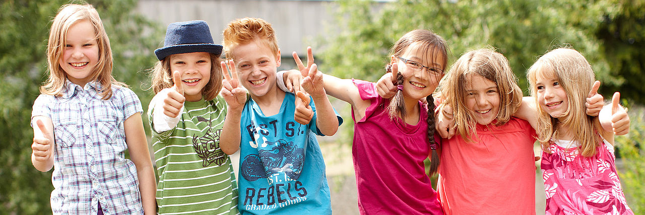 Sechs Kinder stehen lachend in der Natur.