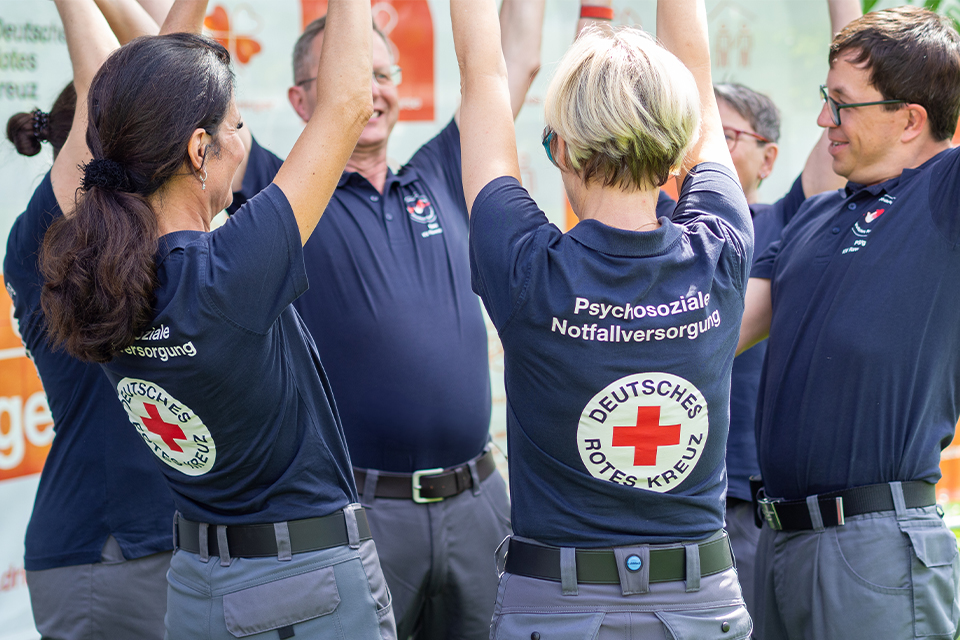 Mehrere DRK-Mitarbeiter stehen zusammen und strecken ihre Hände in die Höhe.