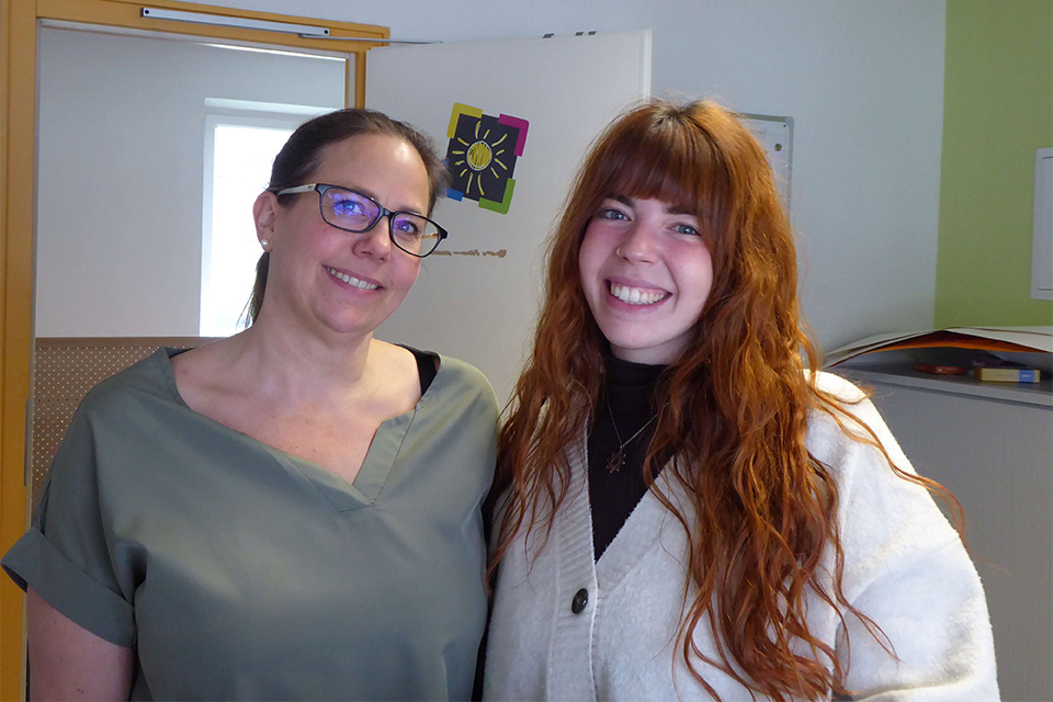 Zwei Frauen stehen in einer Kita zusammen und lächeln in die Kamera.