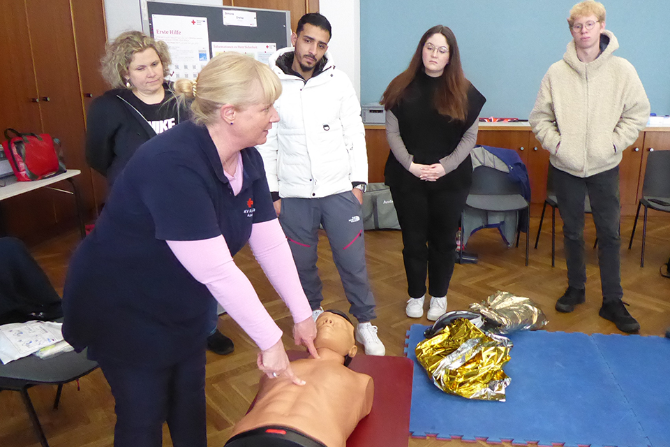 Erste Hilfe Eine Frau zeigt einer Gruppe von Personen Reanimation an einer Puppe.