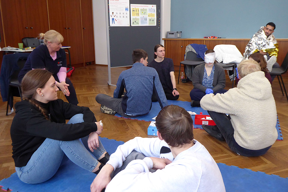 Erste Hilfe Die Teilnehmer eines Erste-Hilfe-Kurses sitzen am Boden.